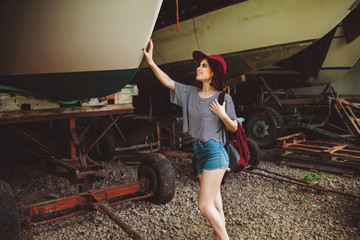 Fototapeta na wymiar Funny Hipster Girl in old boat garage in island, Lots of boats.Trendy Casual Fashion Outfit in summer,spring. Toned Photo.