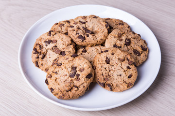 close up of chocolate chip cookies on white plate on wooden tabl