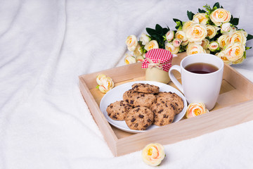 wooden tray with chocolate chip cookies, cup of tea, jam-jar and