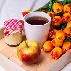 wooden tray with cup of tea, jar of jam or honey, apple and flow