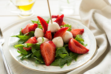 Fresh salad with strawberry, arugula and mozzarella on white plate