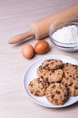 bakery concept - chocolate chip cookies, eggs and flour on woode