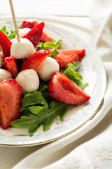 Fresh salad with strawberry, arugula and mozzarella on white plate