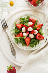 Fresh salad with strawberry, arugula and mozzarella on white plate