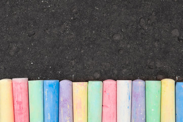 Colorful pastel sidewalk chalk on dark asphalt background. - obrazy, fototapety, plakaty