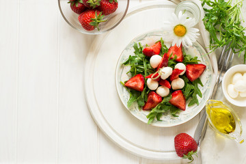 Fresh salad with strawberry, arugula and mozzarella on white plate