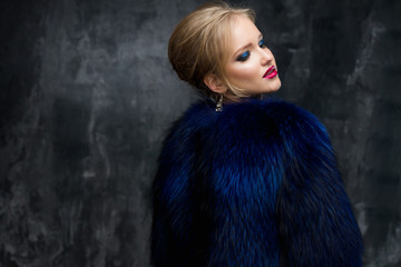 Fototapeta premium Close-up portrait of gorgeous blonde young woman in celebrity style with perfect make up and hair style wearing blue fur. Fashion beauty photo, dramatic look