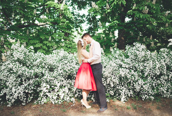 Young beautiful couple kissing and hugging near trees with blossom in summer park