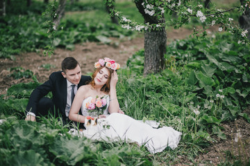 Beautiful bride in a wedding dress with bouquet and roses wreath posing with groom wearing wedding suit. Wedding day