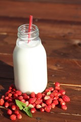 wild strawberies and mint against bottle of milk outdoor. Focus on berries