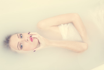 kissing spa finger: portrait of lying in the milk water beautiful tender young blond woman having fun posing sensually & looking at camera on light copy space background