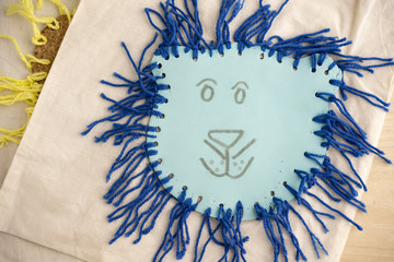 High Angle Still Life of Children Craft of Blue Lion Face with Tied Yarn Mane on Table Top with Copy Space