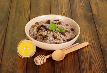 Bowl oatmeal with raisins, honey, spoons on dark wooden background.