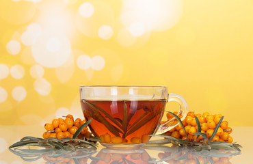 Fruit tea made from buckthorn in cup on abstract yellow.