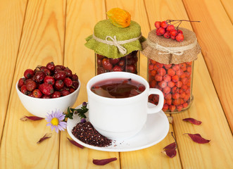Cup fruit tea, jars with berries mountain ash and rosehip.