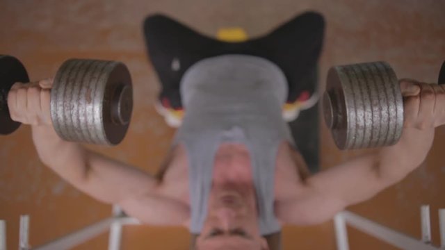 Young athletic man training in old soviet gym. Ungraded. Chest workout with dumbbells