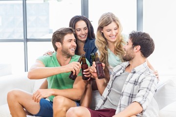Smiling friends sitting on sofa drinking beers