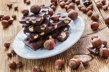 Chocolate and nuts: hazelnuts and pieces of dark chocolate with hazelnuts on white plate on wooden background