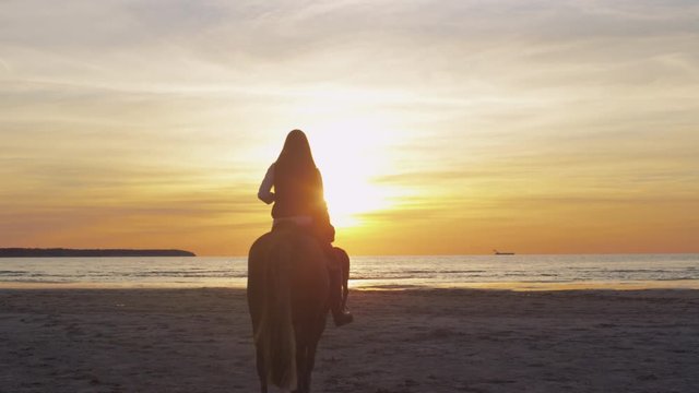 Silhouette of Two Young Riders on Horses at Beach in Sunset Light. Back View.