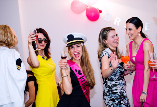 Cheerful bride and bridesmaids celebrating hen party with drinks