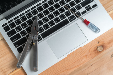 Computer and technology repair suggested by a  handled set of pliers on a silver laptop with black keyboard
