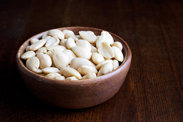 Rustic wooden bowl of peeled whole almonds isolated on dark wood