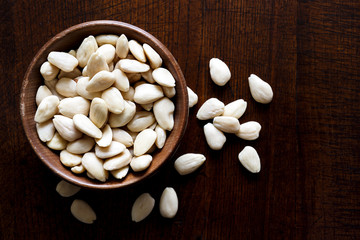 Rustic wooden bowl of peeled whole almonds on dark wood from abo