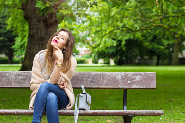 Beautiful young woman sitting on a bench in the sun and smiling
