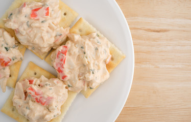Plate of lobster dip on saltine crackers atop wood table