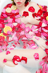 beautiful sexy elegant young lady with red lipstick and silk skin having fun lying in water bath relaxing on colorful rose petals copy space background