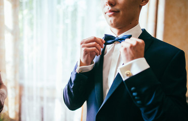 The groom in white shirt put his bow-tie in the morning of the wedding day. Close up photography. Preparation time