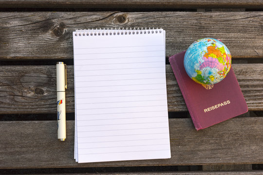 Overhead view of notebook and globe beside passport and pen on rustic wooden table