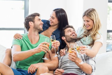 Smiling friends sitting on sofa drinking alcohol