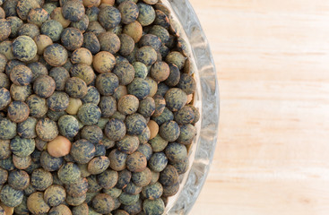 Top close view of green lentils in a small glass bowl on a wood table.