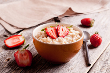 Tasty oatmeal with strawberry on wooden table close-up