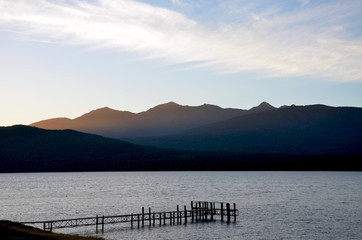 Wispy  clouds at dusk  over Lake Te Anau  and its jetty, surrounded by mountains and pristine wilderness in fiordland, New Zealand