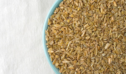 Top close view of cracked freekeh in a bowl on a light beige tablecloth.