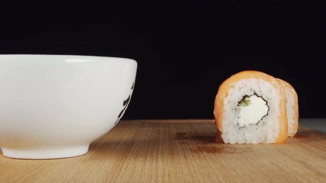 Human hand takes a sushi by chopsticks from a plate and dip it in a sauce cup