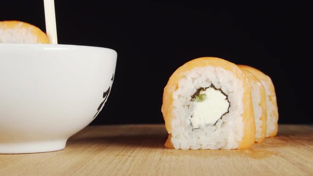 Human hand takes a sushi by chopsticks and dip it in a soy sauce