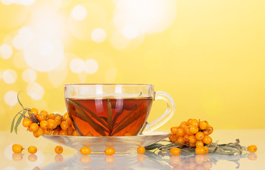 buckthorn berries and cup fruit tea on abstract yellow background.