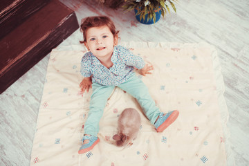 Naklejka premium The little red-haired girl playing with rabbit in the room. The concept of happiness, joy and family values