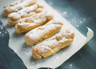 Cakes eclairs with powdered sugar on parchment paper on grey wooden background