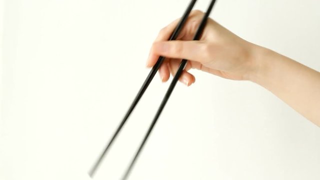 Demonstrating uses of chopsticks against white background 