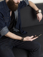 Young bearded man using a cell phone at home. Close up. No face.