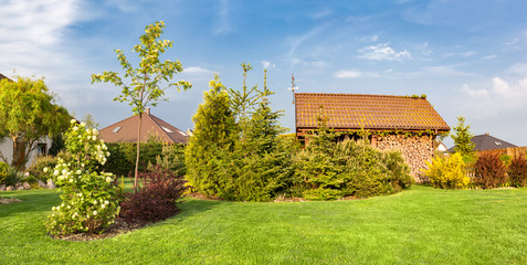 Backyard of a family house. Landscaped garden with green mown grass, wood shelter.