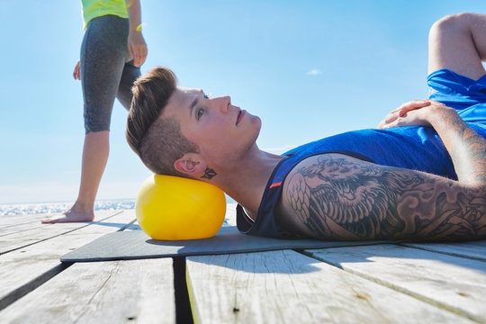 Tattooed man lying on pier using ball as pillow