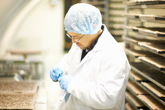 Side view of worker wearing hairnet and latex gloves collecting samples in plastic bag