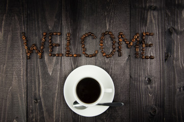 White cup of coffee and a word of welcome from the coffee beans on wooden background