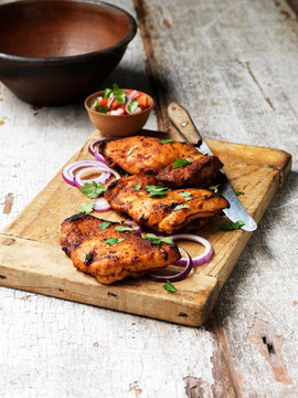 Barbecued tandoori chicken thighs with salad on chopping board