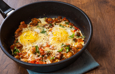 fried eggs with vegetables, mushrooms and cheese in a frying pan on wooden table